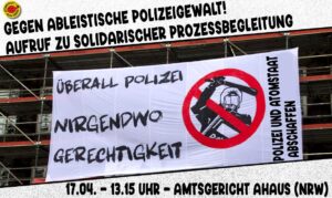 Mit Banner an einer Fassade. darauf steht überall Polizei nirgendwo Gerechtigkeit Polizei und Atomstaat abschaffen. Zeichnung eines schlagenden Polizeibeamten in einem roten durchgestrichenen Kreis. Über das Bild steht gegen ableistische Polizeigewalt Aufruf zur solidarischer Prozessbegleitung. Zu sehen auch eine antiatom Sonne. und termin: 17.04. 13h15 Amtsgericht Ahaus