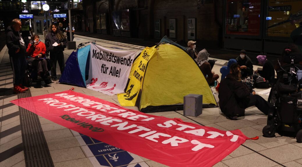zeltlager auf dem Bahnsteig mit Menschen und Banner zu Mobilitätswende für alle